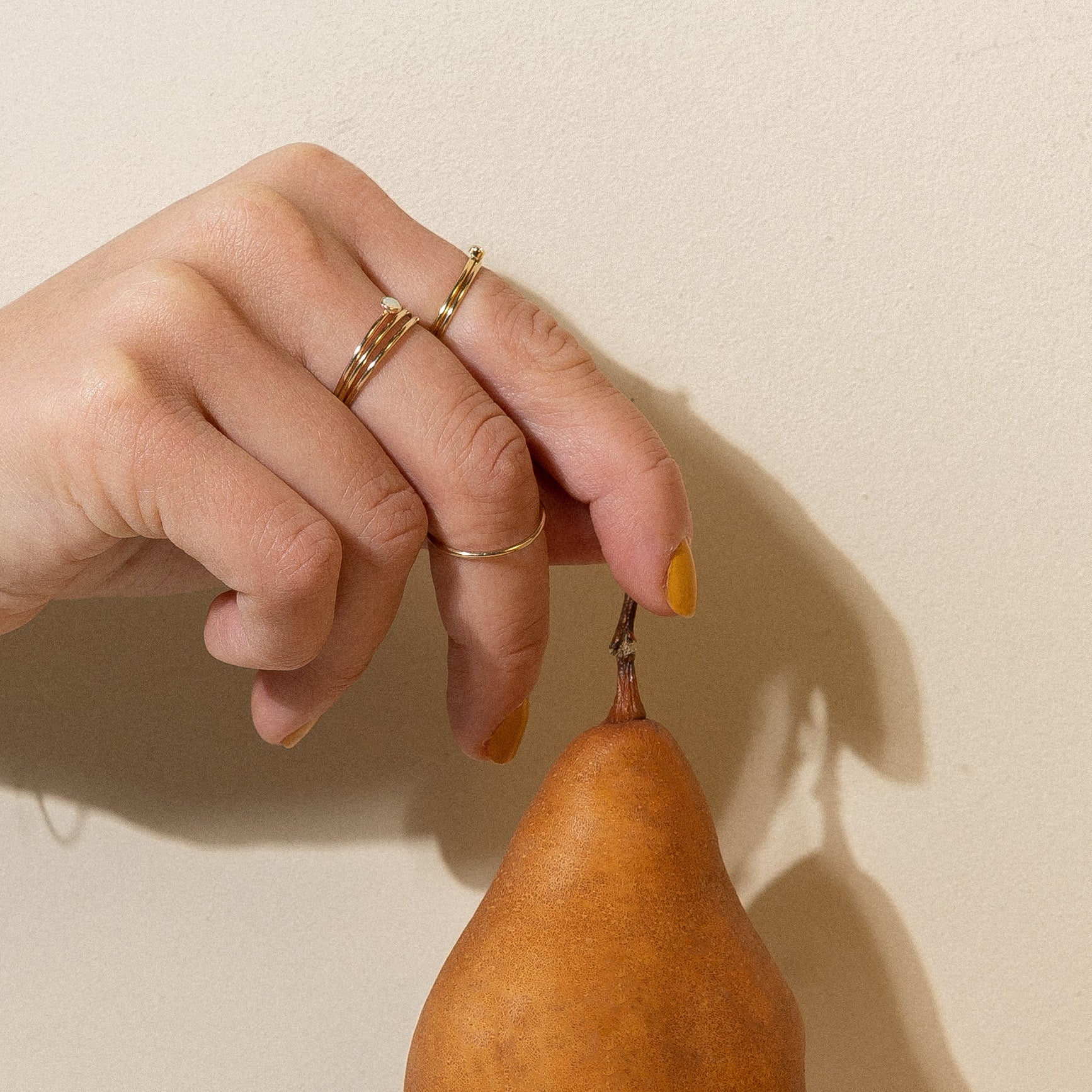 a woman holding 4 gold fine gold ring bands to the camera