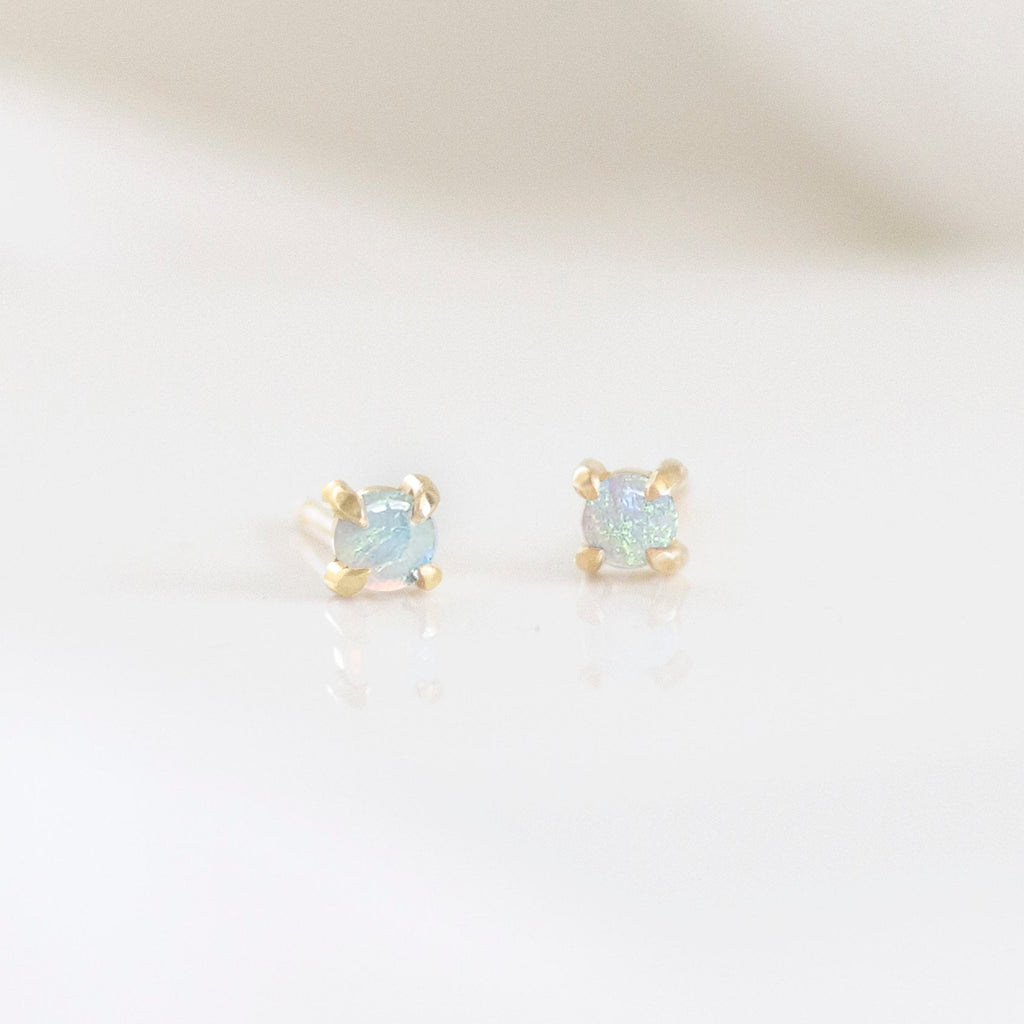 A pair of stud earrings with an Australian opal in a gold setting, placed on a white surface.