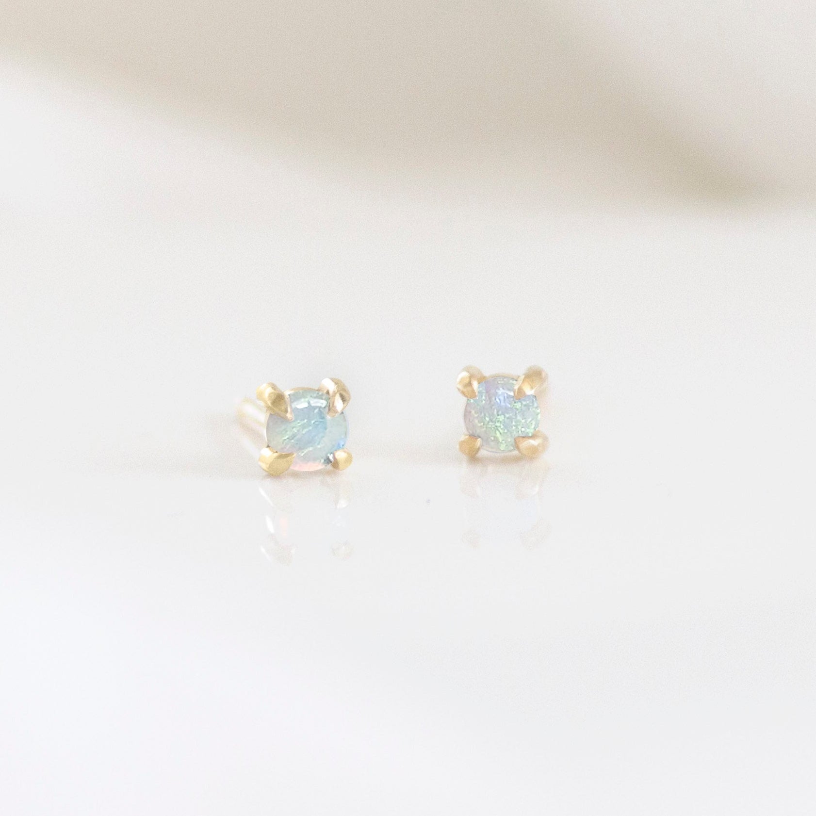 A pair of stud earrings with an Australian opal in a gold setting, placed on a white surface.
