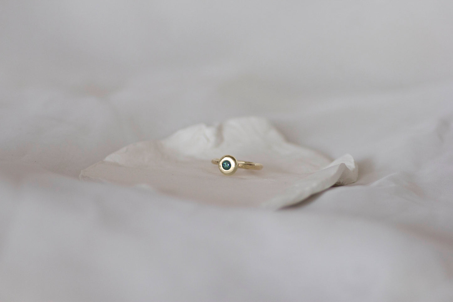 Australian Blue/Green Parti Sapphire set in a heavy, 14ct yellow gold ring sitting on a white ceramic dish by jane finch